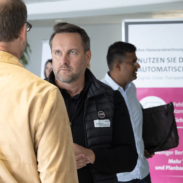 Zwei Männer mittleren Alters, einer davon von hinten, im Gespräch.