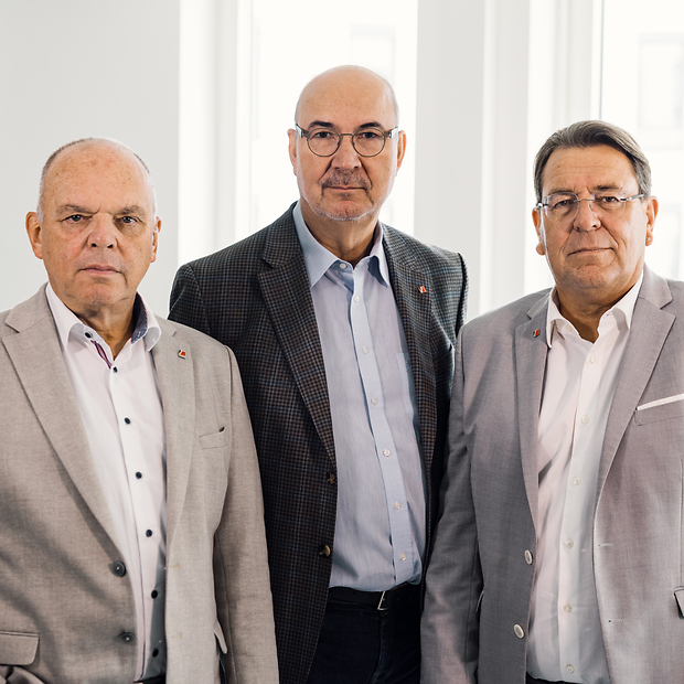 Vorstand der KV RLP 3 ältere Herren in Anzug, nebeneinander stehend, blicken ernst in die Kamera.