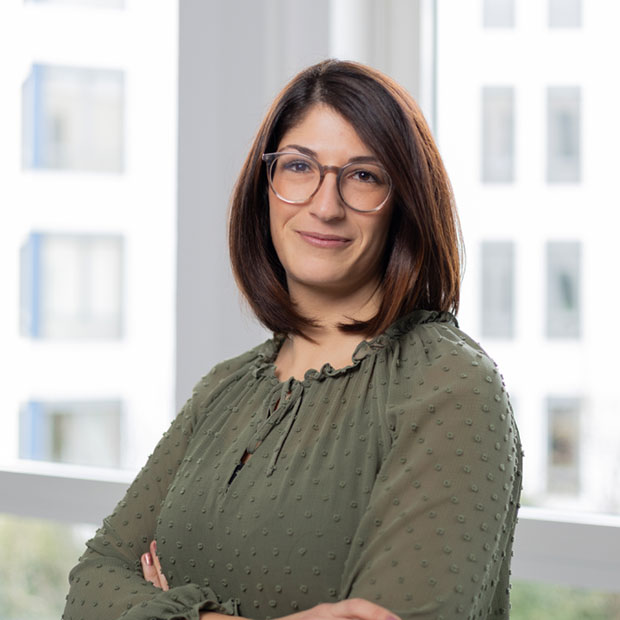 Portrait Sabrina Toscano: mittelalt, schulterlange Haare, Bluse, Brille, Lächeln in Kamera