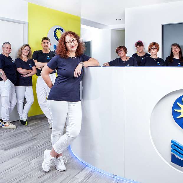 Praxis Sögding-Beck Frau Dr. Sogding-Beck steht mit ihrem Team im Anmeldebereich der Praxis. Alle lächeln in die Kamera.
