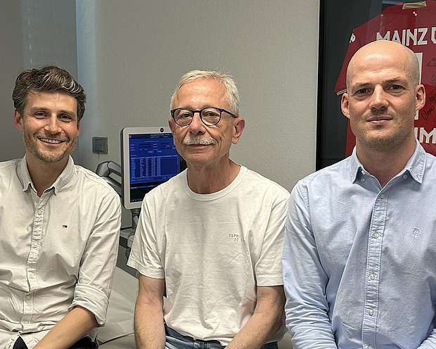 Dr. Alexander Tamm, Dr. Sören Schwuchow-Thonke und Dr. Bernhard Schmitt Zwei Männer mittleren Alters und ein älterer Mann sitzen auf einer Liege in einer Arztpraxis. Alle drei lächeln.