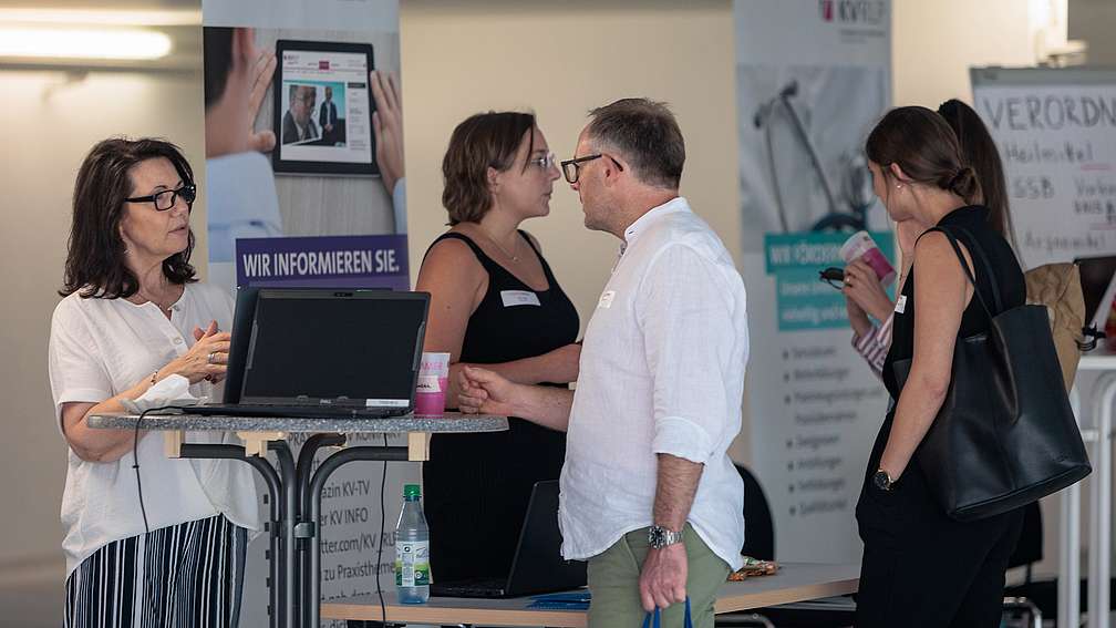 Austausch am Infostand Menschen im Gespräch an Infostand mit Laptop und Broschüren beim Sommerkongress 2023.