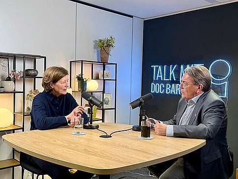 Prof. Dr. Kirsten Müller-Vahl und Dr. Andreas Bartels im "Talk mit Doc Bartels". Eine Frau mittleren Alters und ein älterer Herr sitzen im Gespräch an einem Hochtisch.