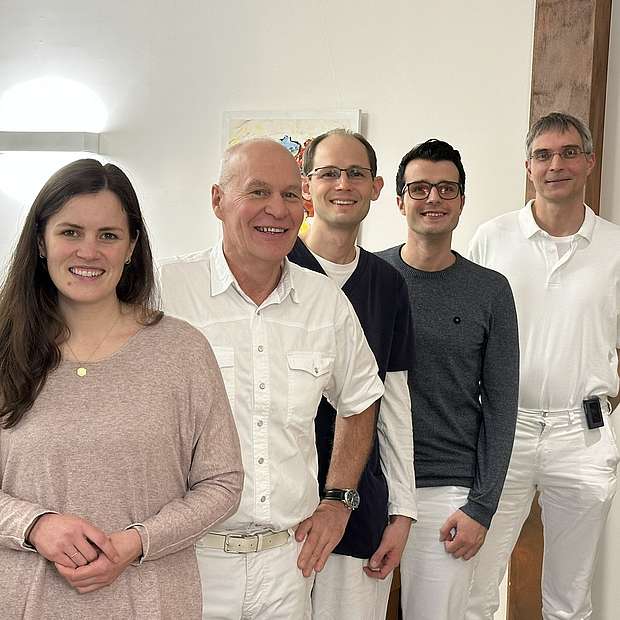 4 Männer und 1 Frau mittleren Alters lächeln in die Kamera.