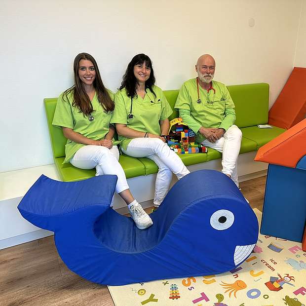 Simone Scheid, Eunike Schulz und Dr. Romain Krier Zwei Frauen und ein Mann sitzen im Wartezimmer einer Kinderarztpraxis.