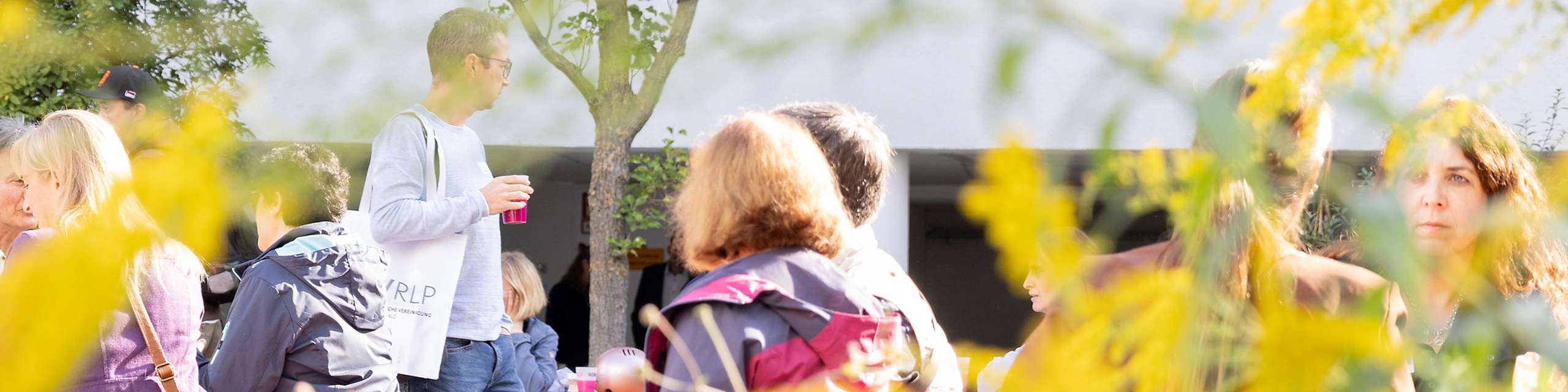 Im Vordergrund Blumen, im Hintergrund Menschen sitzend, laufend.