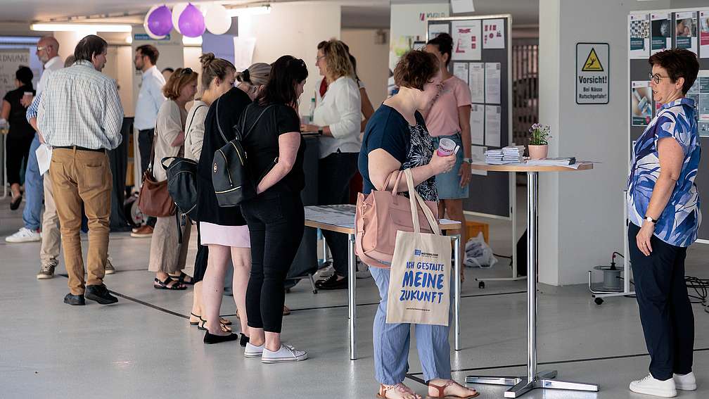 Infostände Sommerkongress 2023 Frauen und Männer stehen in einem großen Raum und informieren sich an Infoständen.